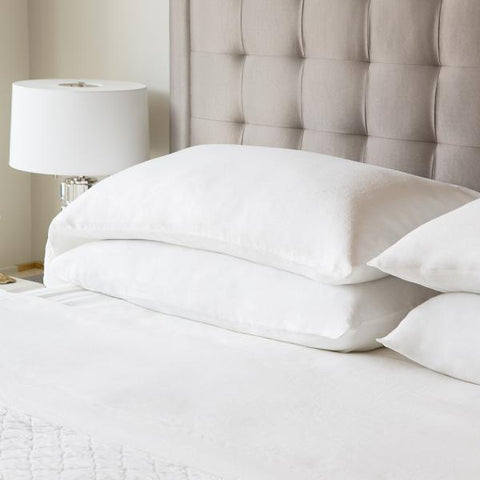 A white Malouf bed with two Malouf Woven French Linen pillows and a lamp on top exudes classic elegance.