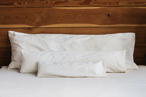 A white bed with Holy Lamb Organics Body Pillows and a wooden headboard for body support.