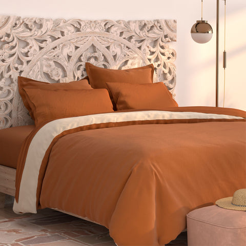 A cozy bedroom featuring an ornate white headboard, burnt orange designer PureCare Pillow Sham Set | Cooling Bamboo covers, a pendant light, and warm neutral tones, exuding modern elegance and comfort.