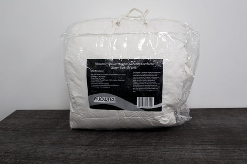 A bag of white bedding, including Pillowtex Classic Weight Feather and Down Comforter, sitting on a wooden table.