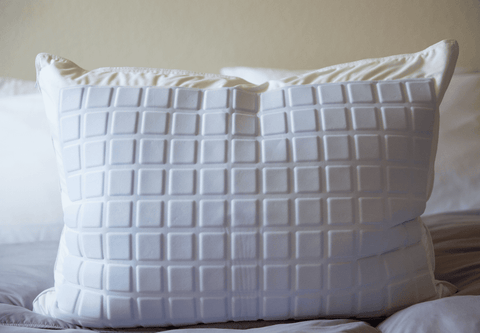 A Pillowtex Cooling Gel Pillow Protector with squares on it on a bed made of 100% cotton.