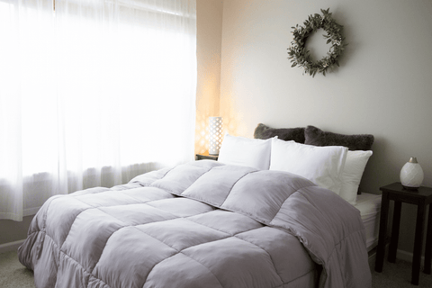 A bed with a grey comforter and a wreath on it, featuring the Pillowtex Essential Bedding Package | All Season Comforter with Matching Pillows.
