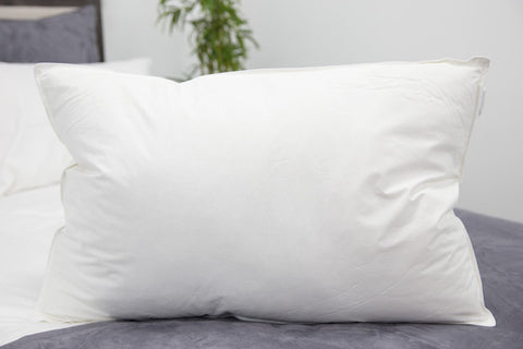 A fluffy Pillowtex Bamboo Bedding Package pillow with bamboo pillow protectors rests on a neatly made bed with gray sheets, accompanied by another pillow in the background, suggesting a clean and inviting bedroom setting.