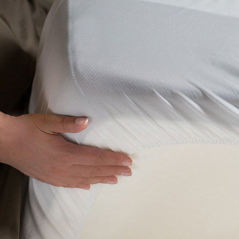 A person is holding a Protect-A-Bed Premium Mattress Protector on a bed.