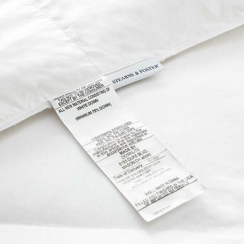 A close-up view of a Stearns & Foster White Down Comforter showing washing symbols, material composition (600 fill power white duck down), and instructions in English with a "made in USA" label.