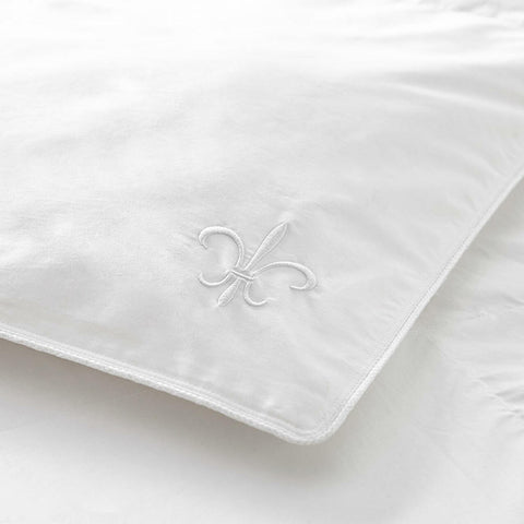 A pristine white Stearns & Foster White Down Comforter with a delicate fleur-de-lis embroidery, symbolizing elegance and crafted from 400 thread count cotton, set against a soft, wrinkled bedding background, suggesting comfort and luxury.