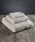 Three 100% Organic Cotton Bath Towels from Delilah Home, soft and plush, are neatly stacked on a rustic wooden surface with a dark gray background, highlighting the inviting texture and luxurious quality of this bath towels collection.