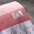 A close-up of a folded Delilah Home 100% Organic Cotton Sunset Beach Towel with red and white horizontal stripes, white fringes, and the brand logo, resting on a gray surface.