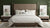 A modern bedroom with a large brown upholstered bed, Delilah Home's Final Sale: Organic Hemp Bed Sheet Collection, white and beige bedding, a green accent wall, two wood nightstands with white tops, round glass lamps, framed art, and an area rug over hardwood floors.