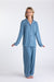 A cheerful woman stands barefoot against a white background wearing the Sleep Again Pillows Long Sleeve Bamboo Pajama Set in light blue. This breathable set features a button-up top and loose pants, perfect for relaxed comfort.