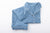 The Long Sleeve Bamboo Pajama Set by Sleep Again Pillows features a light blue, white-trimmed, button-up top with collar and chest pocket, plus matching pants. This soft and breathable set is displayed neatly folded on a white background.