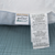 Close-up of a pillow tag with "Manchester Mills" and "Microban" logos, highlighting 100% polyester fibers. Made by Sysco Guest Supply Inc., NJ, USA, in April 2022. This Envirosleep Dream Surrender Firm Pillow is ideal for side sleepers seeking hypoallergenic comfort on a blue quilt.