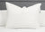 The Pillowtex High End White Goose Down Pillow, featuring a 50% feather and 50% down fill, sits upright on a neatly made bed with a white comforter. A light gray headboard and two more white pillows from Pillowtex are partially visible.