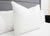 The Pillowtex High End White Goose Down Pillow (50% feather/50% down) stands upright on a neatly made bed with white sheets, next to a gray upholstered headboard and a black nightstand in this minimalistic room.