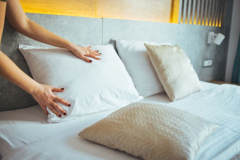 A woman is carefully arranging Woodspring Ecoendure Pillows by Keeco on a bed, featured at Many Choice® Hotels.