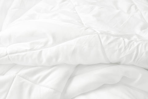 A close-up image of a white, textured Pillowtex Classic Weight Down Alternative Comforter with soft, uneven folds and creases, creating a cozy and inviting appearance. The focus on texture and light suggests a calm, serene atmosphere.