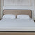 A neatly made bed with a beige upholstered headboard features two La-Z-Boy Down Alternative Pillows by La-Z-Boy and a white textured mattress, set against a wall topped with a large neutral-toned abstract painting.