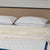 A neatly made bed with a beige headboard features two La-Z-Boy Down Alternative Pillows by La-Z-Boy, each with dark piping and subtle texture, plus a cream knitted blanket folded at the foot.