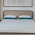 A minimal, tidy bedroom features a beige headboard, two La-Z-Boy Down Alternative Pillows by La-Z-Boy with teal edges, a white textured mattress, and a large abstract white painting above the bed.