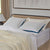 A neatly made bed features two La-Z-Boy Serene Foam Hybrid Pillows with moisture-wicking covers, a cream knit blanket, and white sheets. A beige upholstered headboard, lamp, and abstract art complement the soothing neutral tones.