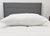A firm, plush JS Fiber "Ultra Down" Polyester Pillow rests on a white mattress before a modern dark gray headboard. The minimal, neutral scene emphasizes the machine washable pillow by JS Fiber.