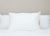 The Best Western® Dreammaker Gusseted Pillow by HD Supply, offering medium-firm support, sits upright on a neatly made bed with a white comforter. A visible orange and gray tag accents the minimalistic setting against a light beige wall.