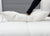 A hand presses on the Pillowtex High End White Goose Down Pillow with medium-firm support, showing its softness—ideal for side and back sleepers—on a white bed with a tufted headboard in a clean, modern setting.