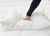 A hand in a black sleeve presses down on the Pillowtex High End White Goose Down Pillow | Medium-Firm Support, forming deep folds in its plush white surface to demonstrate the Pillowtex pillow's comfort for side and back sleepers.