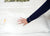 A person wearing a navy blue long-sleeve shirt presses their hand into the Best Western® Dreammaker Gusseted Pillow by HD Supply, showing its medium-firm support. The pillow sits on a white quilted mattress with a floral-patterned pillow behind it.