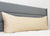 A long body pillow in a Pillowtex Body Pillow Cover | Antimicrobial Copper Infused Bamboo rests against a gray headboard on a white quilted mattress, creating a minimal modern bedroom look with plain white walls.