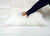 A hand presses down on the Creative Bedding Fossfill Pillow | Antibacterial, showing its softness. The person wears a navy long-sleeved top. The pillow rests on quilted white bedding from Creative Bedding, creating a clean, cozy look.