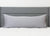 A long, rectangular gray body pillow with the Pillowtex Body Pillow Cover | Antimicrobial Copper Infused Bamboo rests against a gray headboard. The bed's white quilted comforter and plain white wall complete the clean, minimal bedroom look.