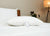The Pillow Factory Housekeeper's Choice Heavenly Spiral Pillow, featured at many Borgata Hotel Casino & Spa®, rests on a white bed set, with a wooden headboard and soft lighting, bringing a hotel-quality touch to your room.