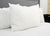 A close-up of a neatly made bed features three Pillowtex Triple Core Lyocell Pillow | Medium Support by Pillowtex against a light gray headboard. Crisp white bedding and pillowcases complete the modern, minimal look.
