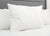 The Pillowtex White Goose Down & Feather Pillow (75% feather/25% down) is propped up with other white pillows on a neatly made bed with a gray upholstered headboard, creating a clean, soft, hotel-inspired look.