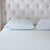 A neatly made bed with a textured white mattress, two La-Z-Boy Fiber Density Pillows with beige piping, and a tall, tufted light beige headboard featuring button details for a clean, minimal, and inviting look.