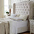 A neatly made bed with a tall, tufted beige headboard is flanked by two white nightstands. The bedding is white and cream with layered pillows, including the La-Z-Boy Hybrid Bliss Memory Foam | Richloft Fiber Foam Core Pillow. Light streams in beside a lamp.