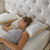 A woman with curly hair sleeps on her side, looking relaxed and comfortable. She rests her head on a La-Z-Boy Hybrid Bliss Memory Foam | Richloft Fiber Foam Core Pillow with beige edges, while another moisture-wicking pillow lies nearby.