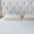 Two rectangular La-Z-Boy Hybrid Bliss Memory Foam Pillows with white, moisture-wicking covers and beige sides rest side by side on a textured white mattress. A light tufted headboard with button details is in the background.