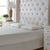 A neatly made bed with a tall, tufted beige headboard features two La-Z-Boy Hybrid Bliss Memory Foam Pillows with moisture-wicking covers and a white mattress, plus white nightstands, a wood lamp with white shade, a plant, and natural window light.