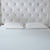 A neatly made bed with a white, textured mattress, two La-Z-Boy Hybrid Bliss Memory Foam Pillows, and a tall, tufted beige headboard with diamond button details creates a clean and minimalistic look.