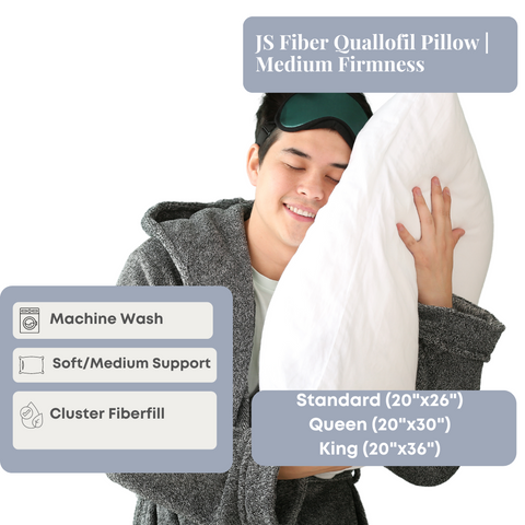 A content young man in a gray robe happily embracing a JS Fiber Quallofil Pillow, highlighting its medium firmness, machine wash capability, and Performa fiberfill, available in standard, queen, and sizes.