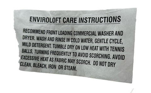 A close-up of a crumpled care label with black text that includes washing instructions for Pillow Factory Enviroloft duvet inserts, specifying machine type, water temperature, detergent type, drying method.