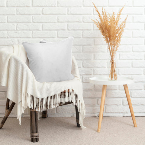 A cozy corner featuring a vintage wooden armchair draped in a soft white throw blanket, with a simple white cushion, now upgraded with a Pillowtex White Duck Feather & Down pillow insert for ultimate comfort, beside a