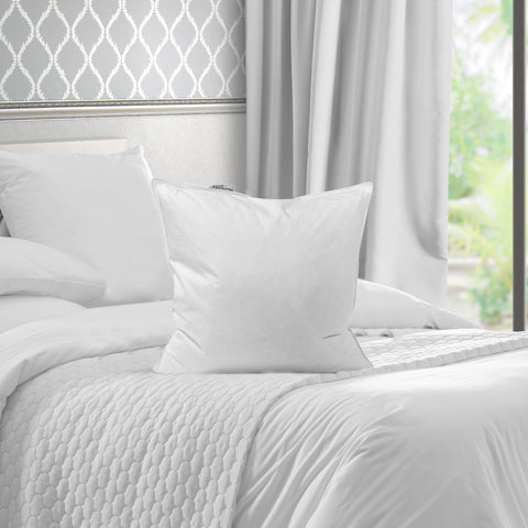 A pristine White Duck Feather & Down Pillowtex pillow insert sits atop a neatly made bed with a textured quilt, framed by elegant gray curtains and a patterned wallpaper, conveying a serene and luxurious bedroom atmosphere.