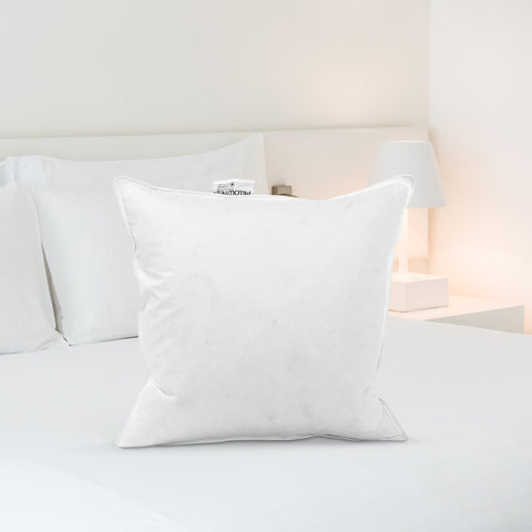 A pristine Pillowtex Pillow Insert filled with White Duck Feather & Down stands against a backdrop of crisp bedding in a brightly lit, minimalist bedroom, exuding a tranquil and inviting ambience for rest.