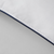 Close-up of a corner of a white pillow with navy blue piping along the edge. The stitching is visible along the seam, reminiscent of the detailed craftsmanship found in the Restful Nights® Euro Box Down Alternative Comforter. The fabric appears smooth and clean, with a subtle shine in the lighting. The background is a plain, light gray surface.