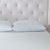 A close-up of a neatly made bed with a white textured mattress, two La-Z-Boy Fiber Density Pillows, and a light tufted headboard. The bedding and headboard create a clean, minimalist, and elegant look.