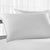 A pristine white Simple Comfort™ Pillow by Suite Sanctuary™ rests atop a matching sheet, suggesting a serene and clean sleep environment, with a subtle backdrop of sheer curtains diffusing daylight.