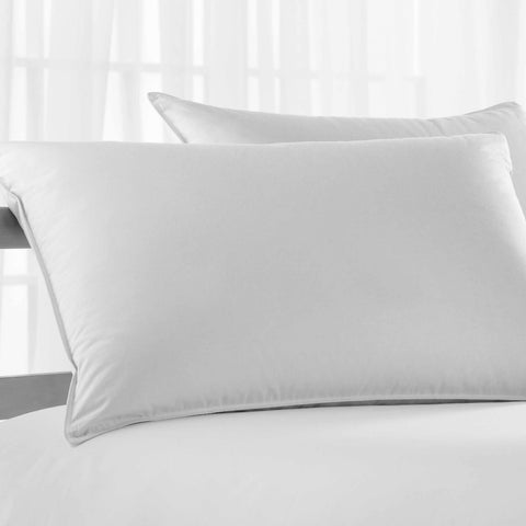 A pristine white Simple Comfort™ Pillow by Suite Sanctuary™ rests atop a matching sheet, suggesting a serene and clean sleep environment, with a subtle backdrop of sheer curtains diffusing daylight.